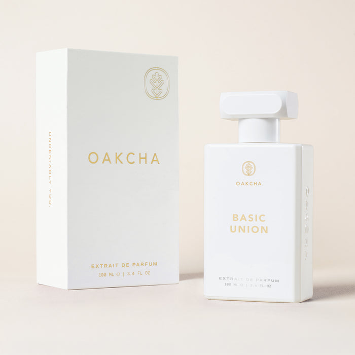 Front view of Basic Union 100 mL perfume bottle and box showcasing gold-foil logo and minimalist white packaging on pale beige background