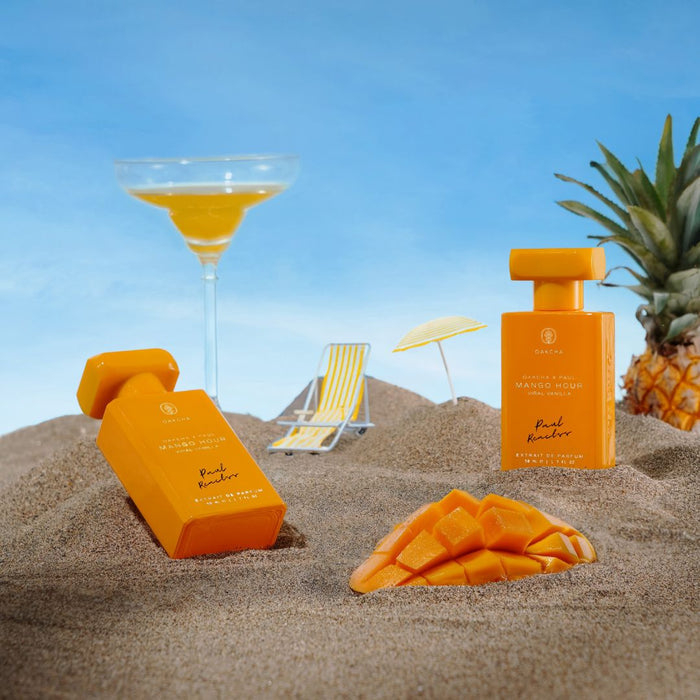 Front of Mango Hour perfume bottle and box showcasing orange packaging with sliced mango on a sandy beach backdrop