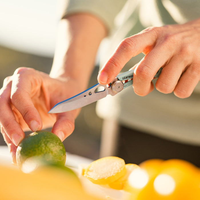 Person using an aqua Skeletool KB folding knife to slice a lime on a cutting surface outdoors.